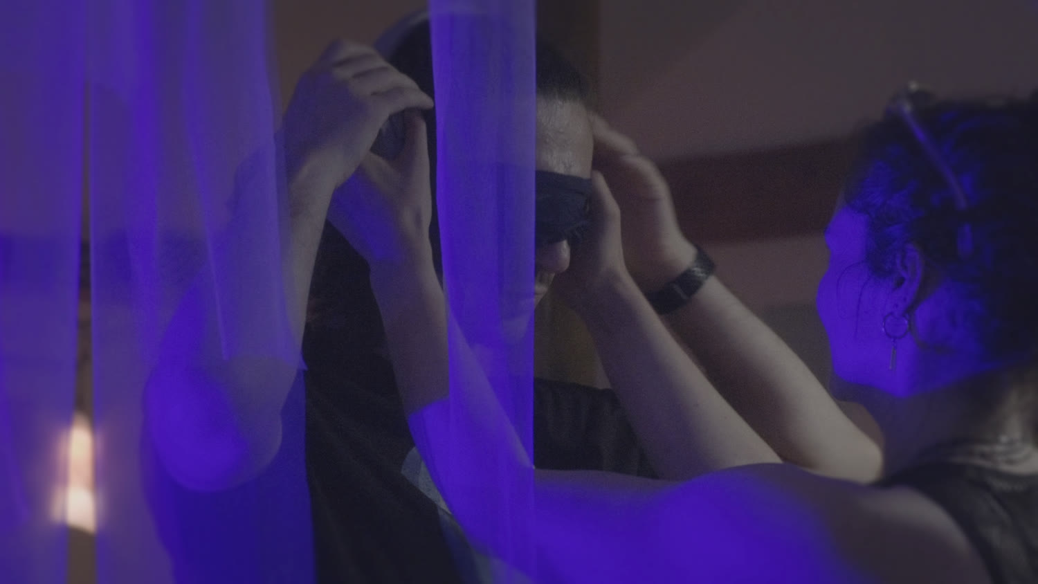 One visitor guiding another's blindfold in blue light